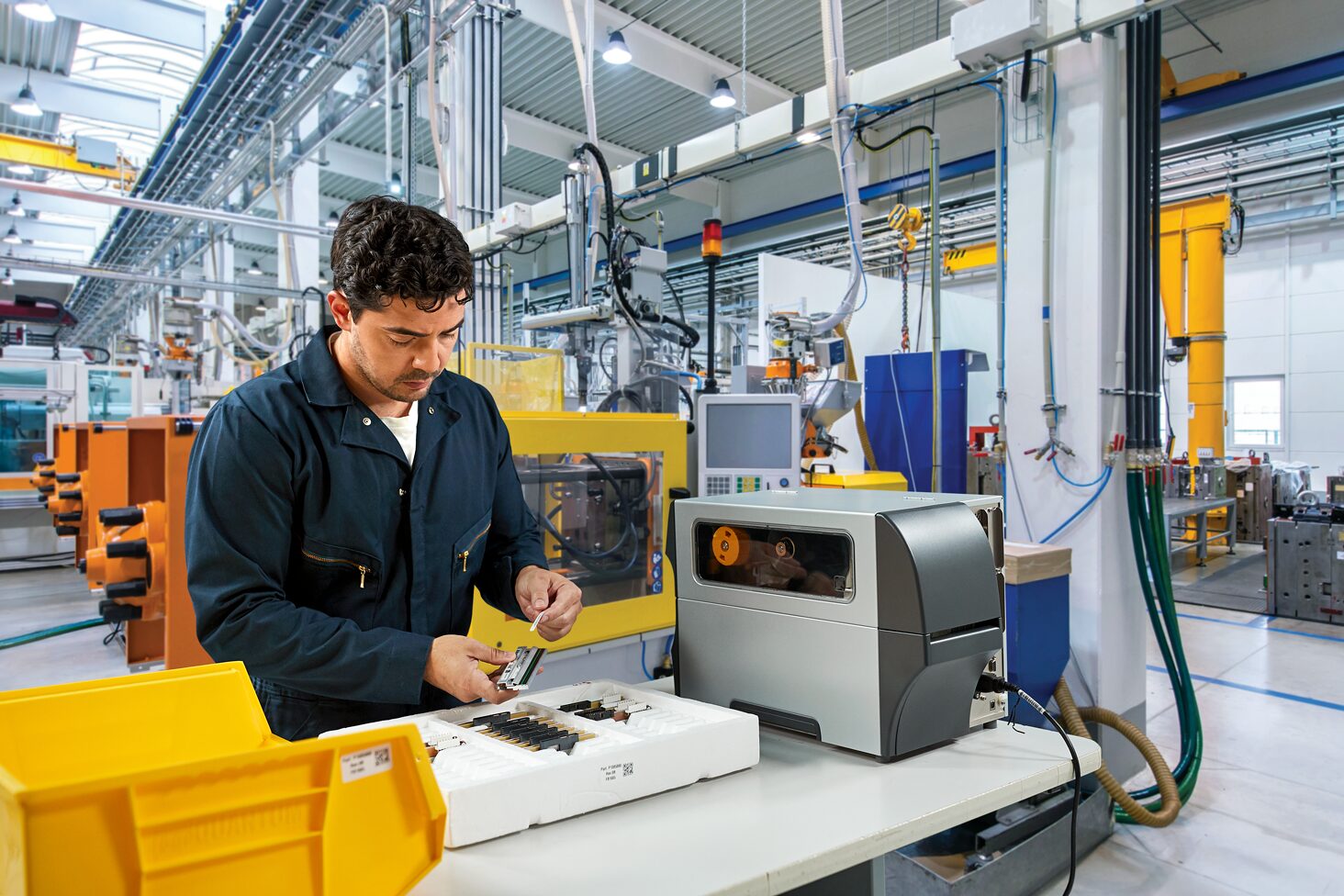 Manufacturing worker applying a component label beside a printer with its supply path visible